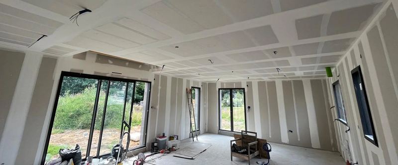 Grande pièce en cours de plâtrerie, plaques posées et joints traités, baies vitrées