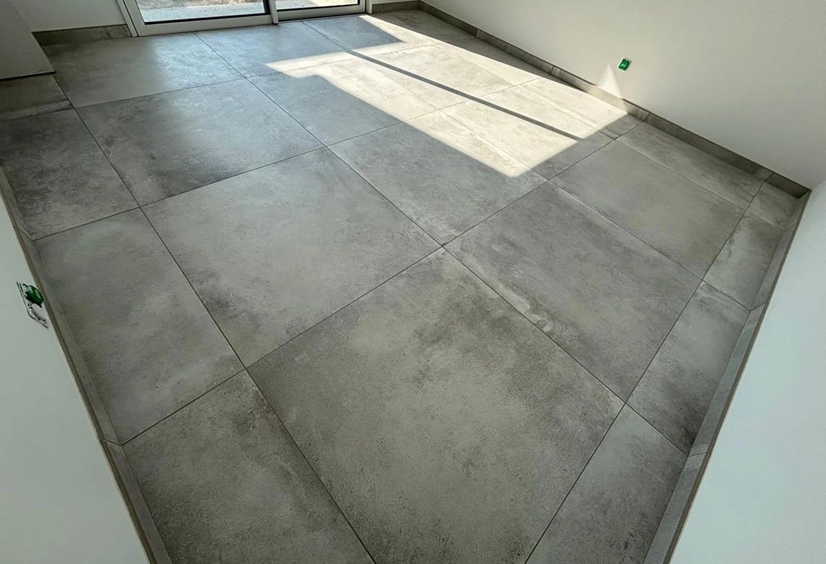 Séjour au sol en carrelage grand format gris, éclairé par une baie vitrée